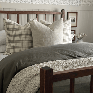 A wooden bed frame, a green blanket, and two Bailey pillows with a Selma centered in front. 