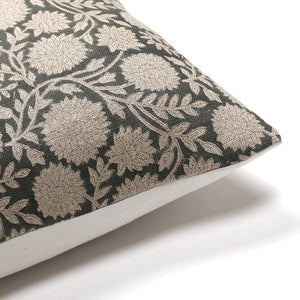 A decorative pillow with a dark fabric cover featuring an intricate floral and leaf pattern in light beige. The corner of the pillow is shown against a white background.