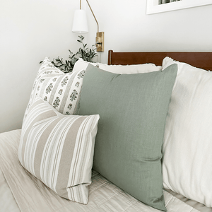 Side view of Colleen pillow cover showing the sage green on the front and back. Paired next to Leighton, Odin lumbar, on a white bed.