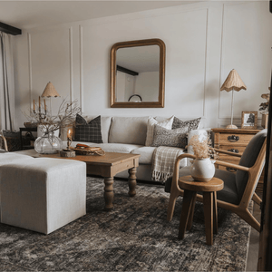 A living room with a gold-framed mirror on the back wall, an ottoman and a wooden coffee table in front of a beige soda with Darcy, Darby, Mavis, Edina, and Madison Lumbar
