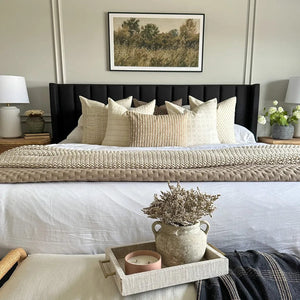 Multiple throw pillows from Colin and Finn on white bed with black headboard. Photo above headboard and stool at end of bed.