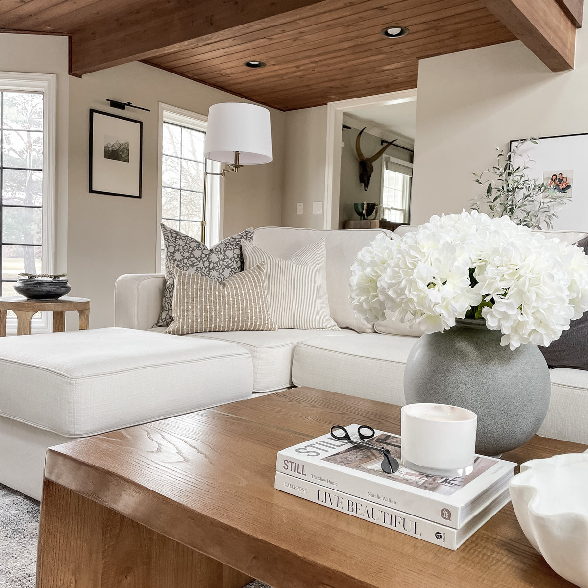 Conyer pillow combination on white sectional sofa with wood coffee table and white florals on it.