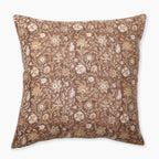 A square decorative pillow featuring a rich rust background adorned with intricate floral patterns in white and gold. The design includes various flowers and leaves, creating an elegant, sophisticated look. The edges of the pillow are clean and neatly finished.