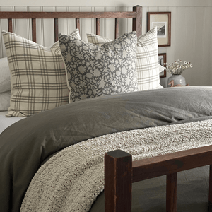 A wooden bed frame, a green blanket, and two Bailey pillows with a Sawyer centered in front. 