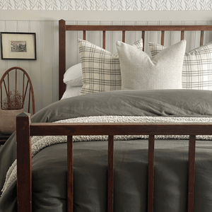 A wooden bed frame, a green blanket, and two Bailey pillows with an Edina centered in front. 