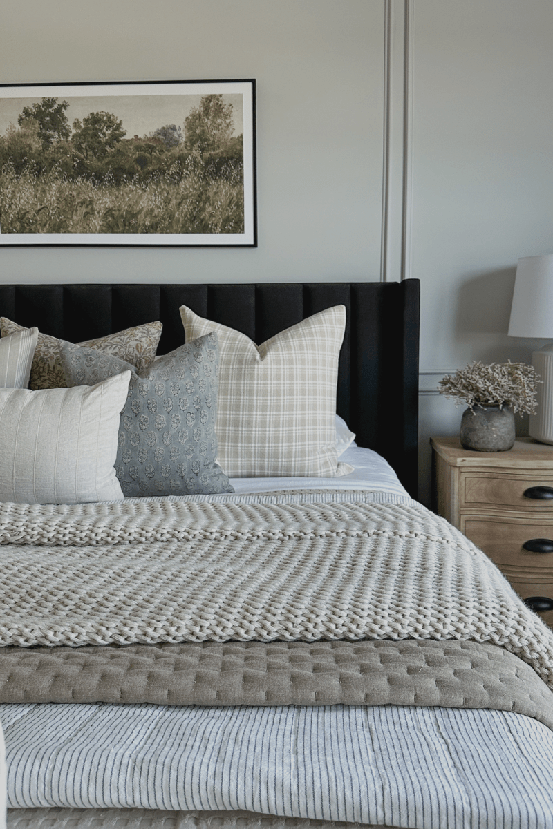 Elain, Eloise, Copeland, and Logan lumbar pillow covers on white bedding with black headboard. Side table is wooden with lamp and faux floral bundle.