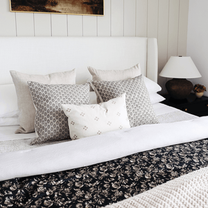 A white bed with two beige pillows, two Ella pillows, and one Dara Lumbar centered in the front