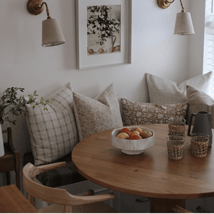 A kitchen nook with Colin + FInn pillows positioned around the table.  Darby, Delilah, Eleanor Natural Lumbar, Selma, and Kinsey. A bowl of fruit, cups, and a pitcher are on the table. 