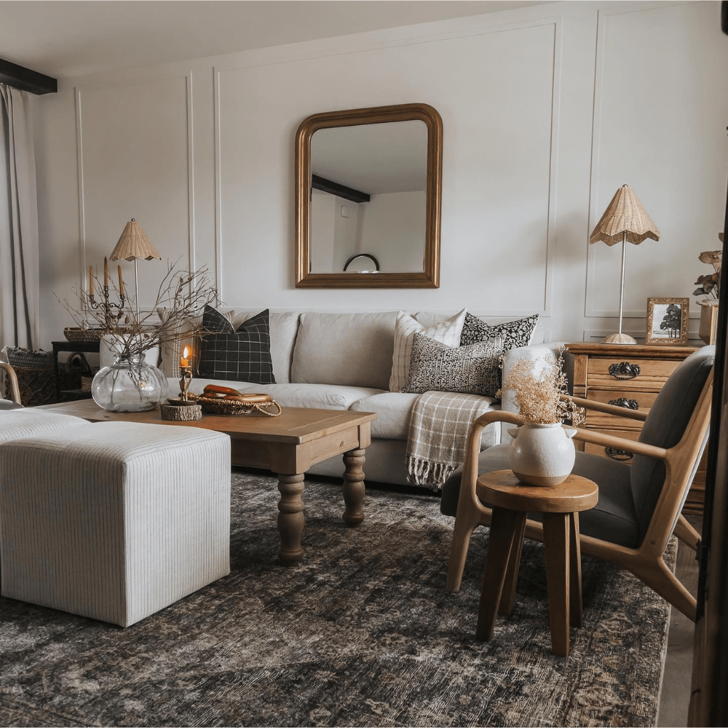 A living room with a gold-framed mirror on the back wall, an ottoman and a wooden coffee table in front of a beige soda with Darcy, Darby, Mavis, Edina, and Madison Lumbar