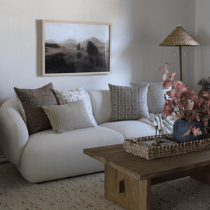 A cream sofa with Emery, Leighton, Isabelle, Louise and Matilda Lumbar in a living room with a wood coffee tale and large canvas behind the sofa