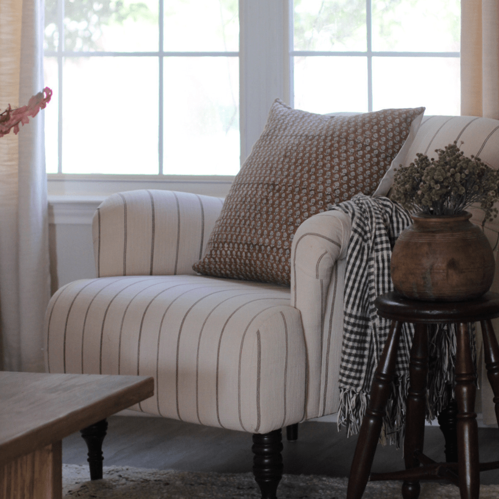 Emery throw pillow from Colin + Finn on a cream striped chair with a stool and plant next to it