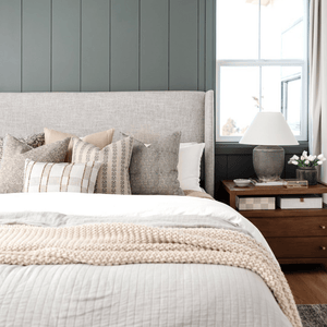 A bed with a gray headboard in front of a green wall. The pillows on the bed are Fitz, Kinsey, Blaine, Eloise, and Royce Lumbar