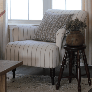 Isabelle from Colin + Finn on a cream striped chair with a stool and potted plant beside it