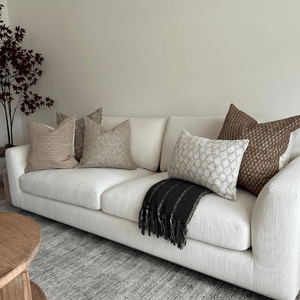 Various Colin and Finn throw pillows on a white sofa with a black throw blanket.