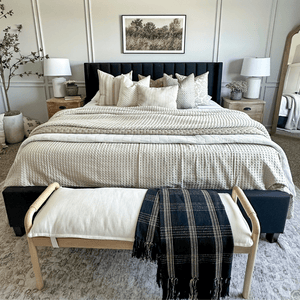 A bed with a black headboard covered in throw pillows and neutral blankets. Throw pillows are from Colin and Finn - Odin, Emberly, Delsi, Odette, Beatrice, and Laney Lumbar.