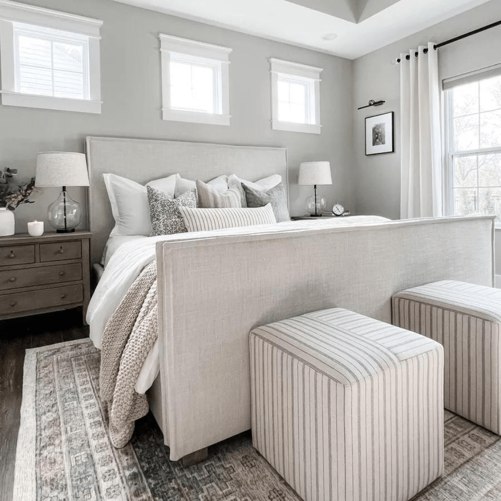 A bedroom with a gray bed in the center of the room with Penelope, Felicity, Eloise, and Winston Lumbar. Two striped ottomans at the foot of the bed. 