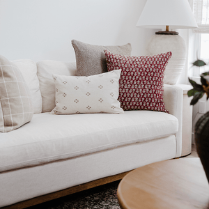 Three pillows, Waylon, Serena, and Dara Lumbar 14x20 are in the corner of a cream colored sofa with a cream colored lamp in the background. 