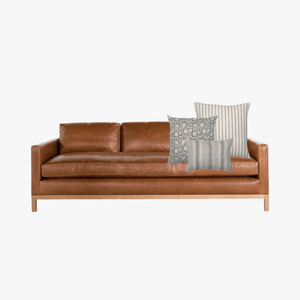 Alice pillow combination on the right side of a faux leather sofa mockup with wooden legs on a white background.