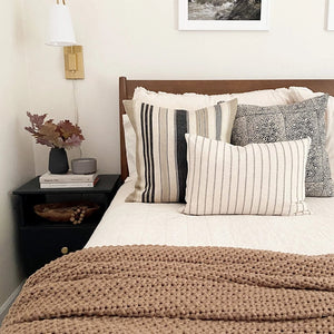 Benedict, Anderson, and Winston lumbar pillow covers from Colin and Finn on white bed with floral arrangement with leaves on side table.