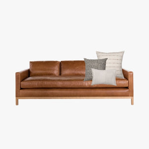 Leather couch with Colin and Finn's Greyson pillow combination on a white background.