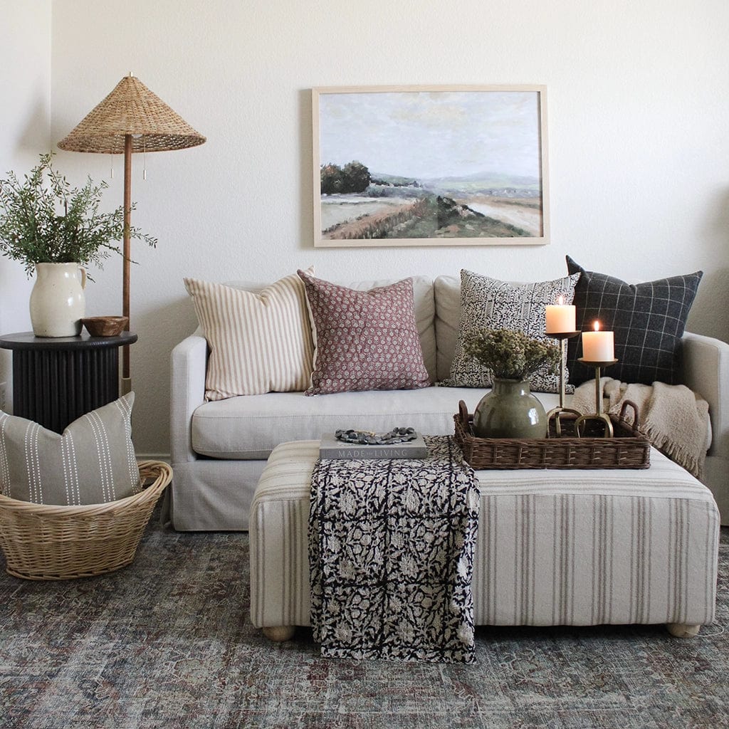 Leo throw pillow on a light grey sofa with Serena, Madison, and Mavis throw pillows. Fabric ottoman with other home decor items.