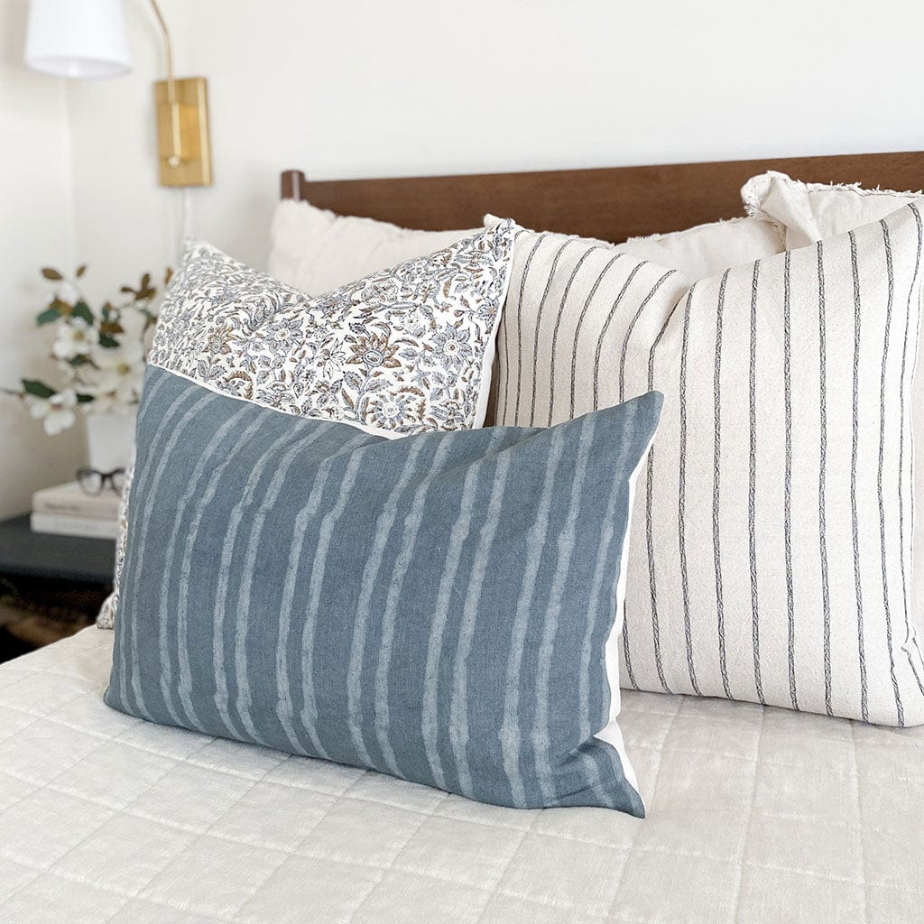 Side view of Penelope, Winston, and River lumbar pillow covers from Colin and Finn on cream bed with wood headboard, sage green blanket, gold sconce, and floral arrangement on side table.