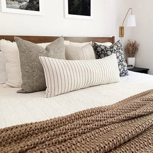 Sidney pillow combination from Colin and Finn on white bed with brown throw blanket and side table with gold sconce.