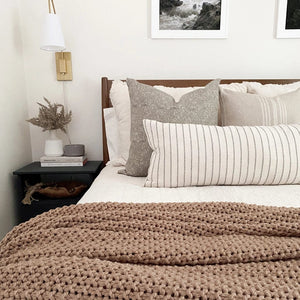 Sidney pillow combination on bed with floral arrangement on side table and brown throw blanket.