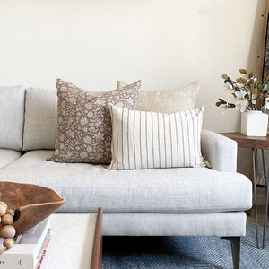 Spencer Pillow Combination including Weston, Eleanor in natural, and Winston lumbar pillows from Colin and Finn on white sofa with floral arrangement on side table.