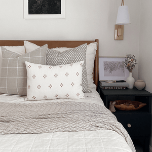 Remy, Wesley, and Dara lumbar pillows on white bed with end table containing books and flowers.